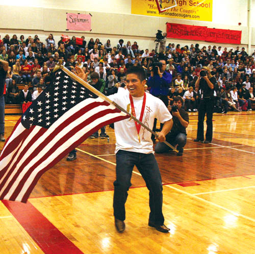 Wearing his Olympic gold medal and waving the American flag he carried into the Coronado High gymasium, �06 
graduate Henry Cejudo grins at family members while students cheer and media members photograph him Oct. 28 during a school assembly in his honor.
Westside Pioneer photo