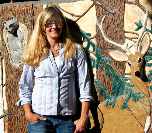 IClay sculptor Sherry Bennett poses in front of part of the
wall outside her house that she�s overlaid with nature
scenes, including the full-relief heads of a raccoon and a deer.
Westside Pioneer photo